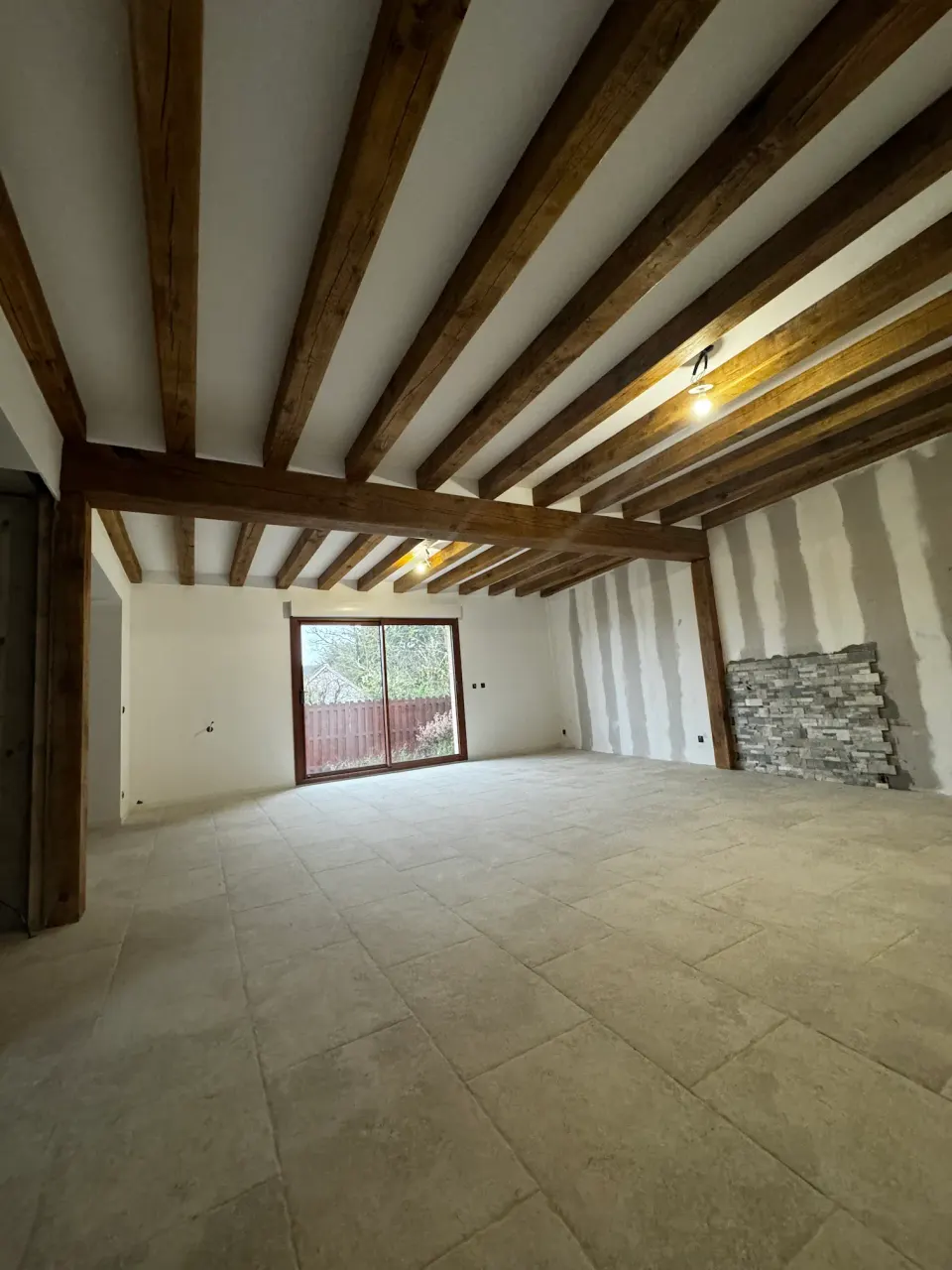 Pièce rénovée avec poutres apparentes, carrelage et mur en pierre